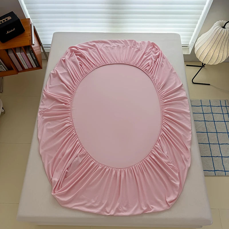 A pink adjustable fitted bed sheet cover is displayed on a white bed frame.