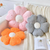 A collection of plush daisy flower throw pillows in shades of pink, gray, and orange resting on a cream knitted blanket.