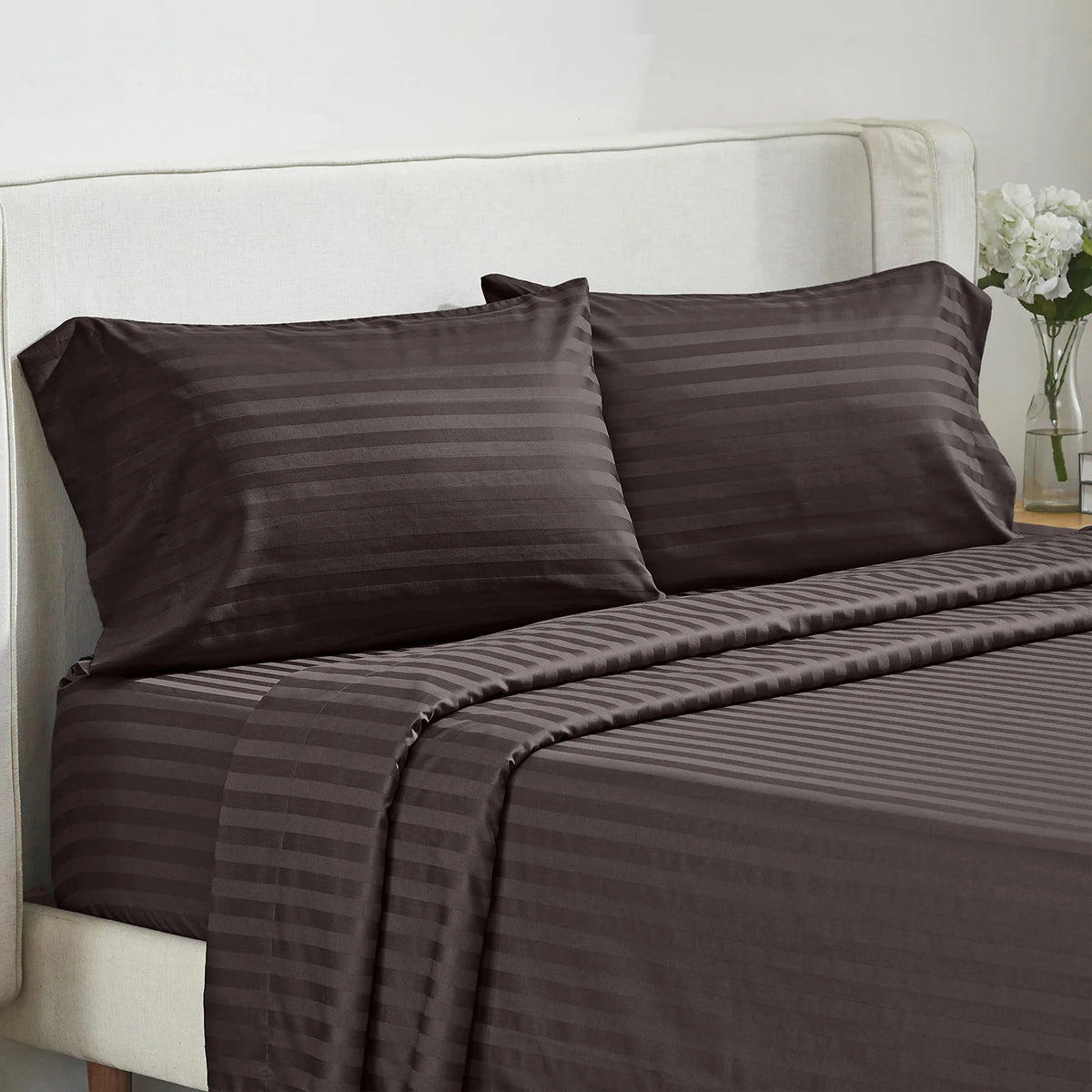A dark brown striped bedding set featuring two pillows and a fitted sheet on a white upholstered bed.