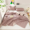 A light pink quilted quilt set with matching pillows and a blanket displayed on a white bed.