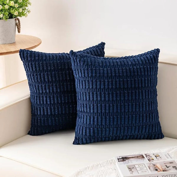 A set of two dark navy blue, textured knit throw pillows resting on a white surface.