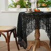 A black lace tablecloth is draped over a wooden table, set for dining with fruit and a candle.