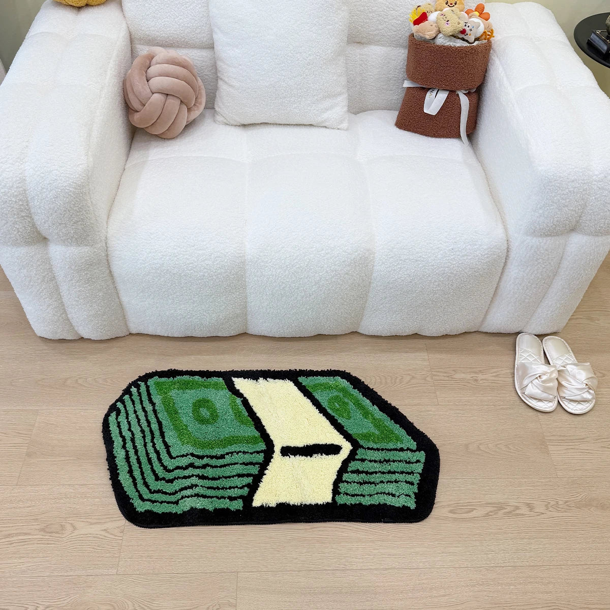 A green and yellow cartoon dollar shaped rug is placed on a light wood floor in front of a white tufted sofa.