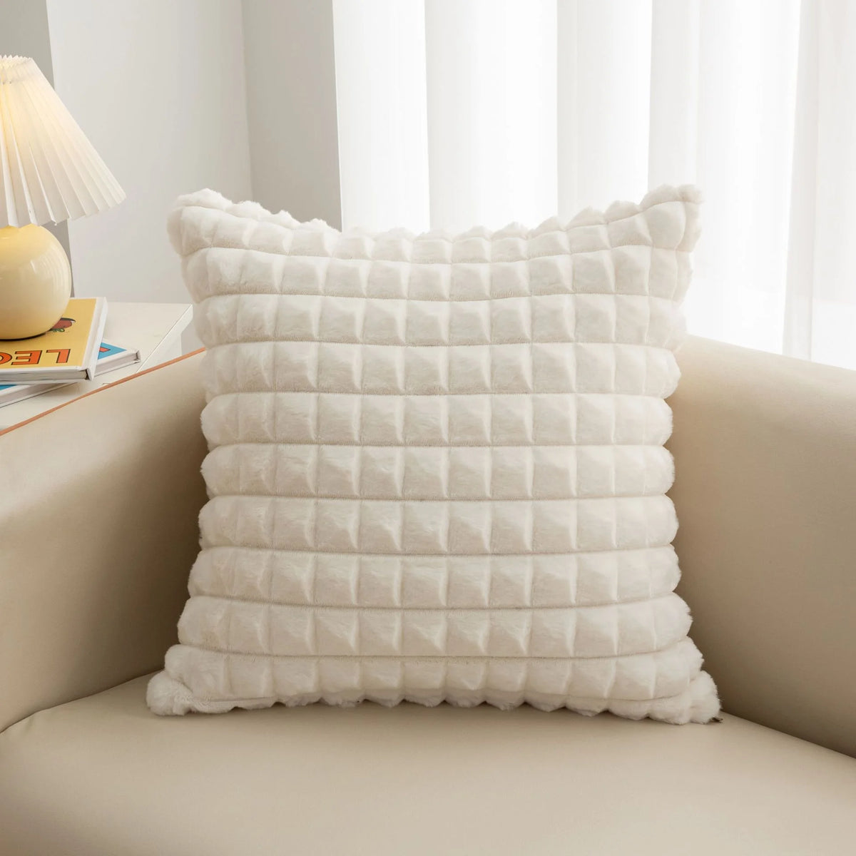 A white, quilted plush winter throw pillow cover resting on a light-colored sofa.
