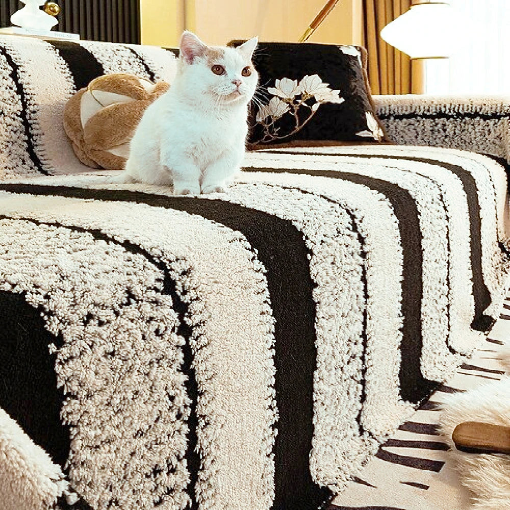 A white cat sits on a black and cream striped fabric surface.