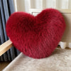 A deep red, heart-shaped plush throw pillow made of fox fur resting on a light-colored surface.