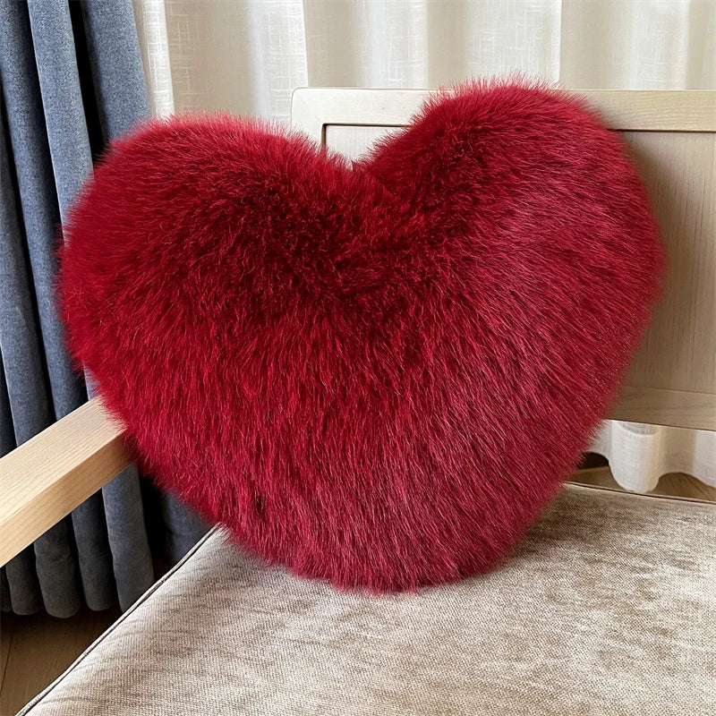 A deep red, heart-shaped plush throw pillow made of fox fur resting on a light-colored surface.