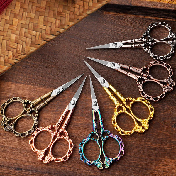 A collection of various crafting scissors in different finishes including silver, gold, rose gold, and iridescent colors on a