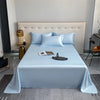A bed dressed with light blue luxury bamboo flat sheets and white pillows against a neutral wall.