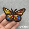 A hand holds a detailed embroidered butterfly patch featuring brown, yellow, red, and blue colors.