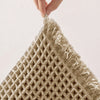 A close-up of a beige non-slip waffle bath mat being held by a hand.