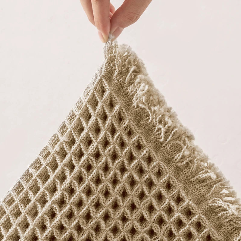 A close-up of a beige non-slip waffle bath mat being held by a hand.