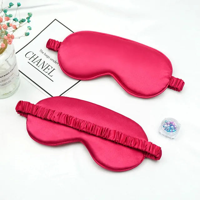 A bright pink silk sleep mask shaped like a curved ear, displayed on a white background.