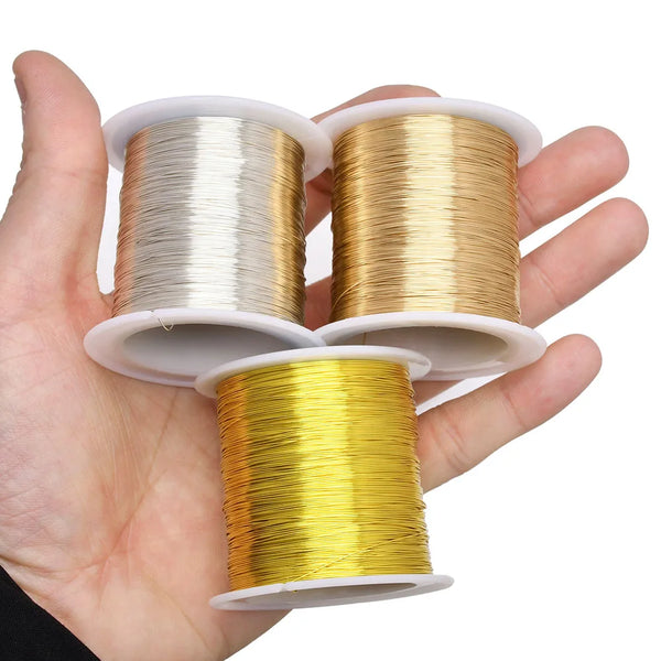 A hand holds three spools of bendable copper clad steel wire in silver, gold, and yellow colors.