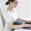 A woman wearing glasses sits at a desk using a laptop while resting her head on a memory foam U-shaped travel neck pillow.