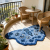 A blue and white irregular shaped plush floor rug sits on a light-colored floor near a balcony with wicker furniture.