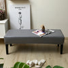 A gray waterproof stretch dining bench cover is displayed on a wooden floor.