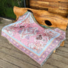 A pink and purple bohemian geometric throw blanket draped over a wooden log.