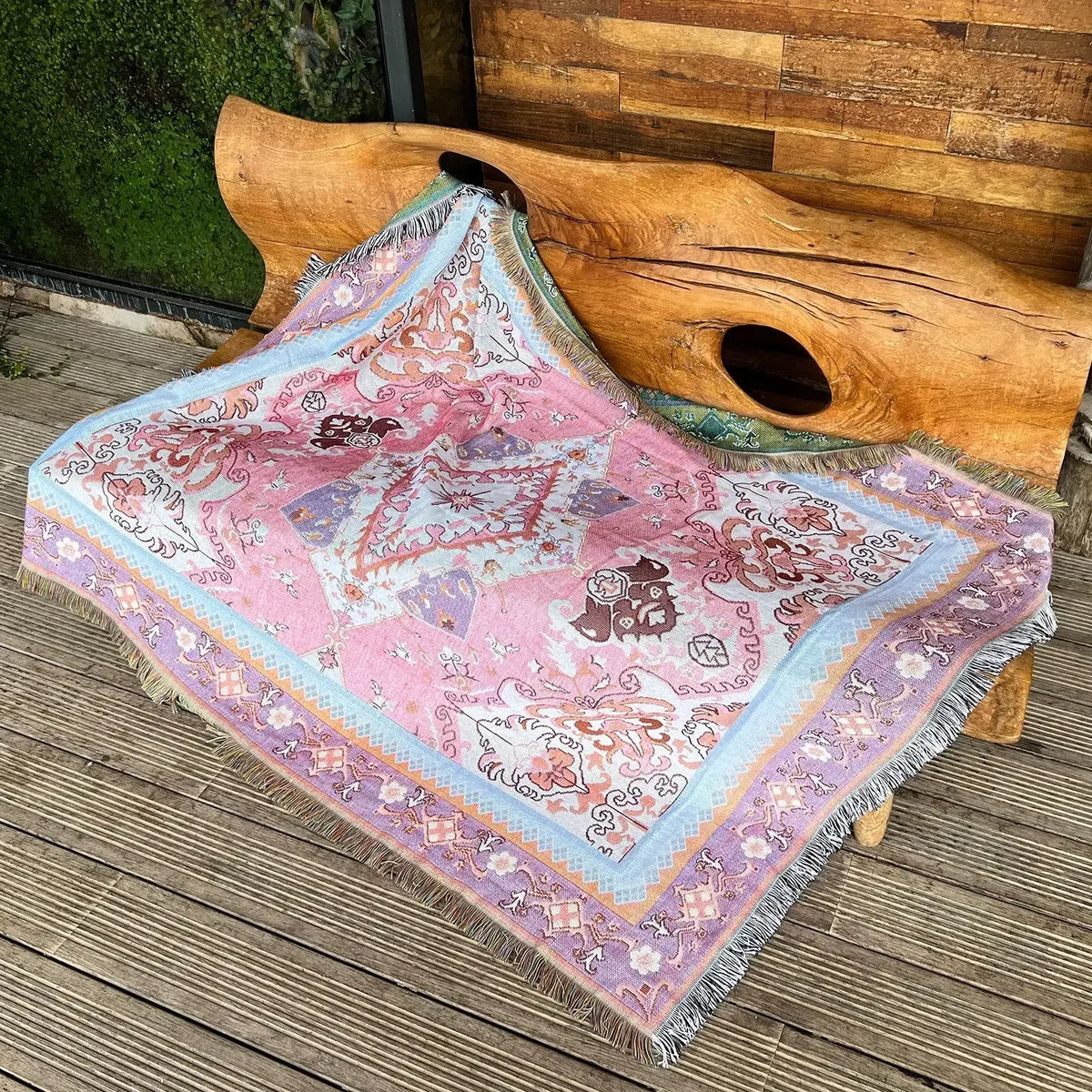 A pink and purple bohemian geometric throw blanket draped over a wooden log.