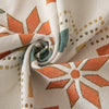 A close-up of a beige fabric with an orange geometric pattern and gold accents, rolled into a swirl.