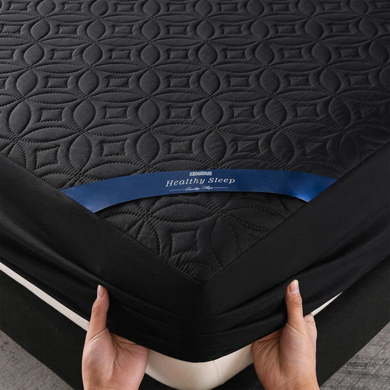 A hand is holding a black quilted mattress protector with the Healthy Sleep brand label visible.