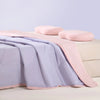 A light pink ice silk summer cooling blanket is draped over a bed with soft pink pillows.