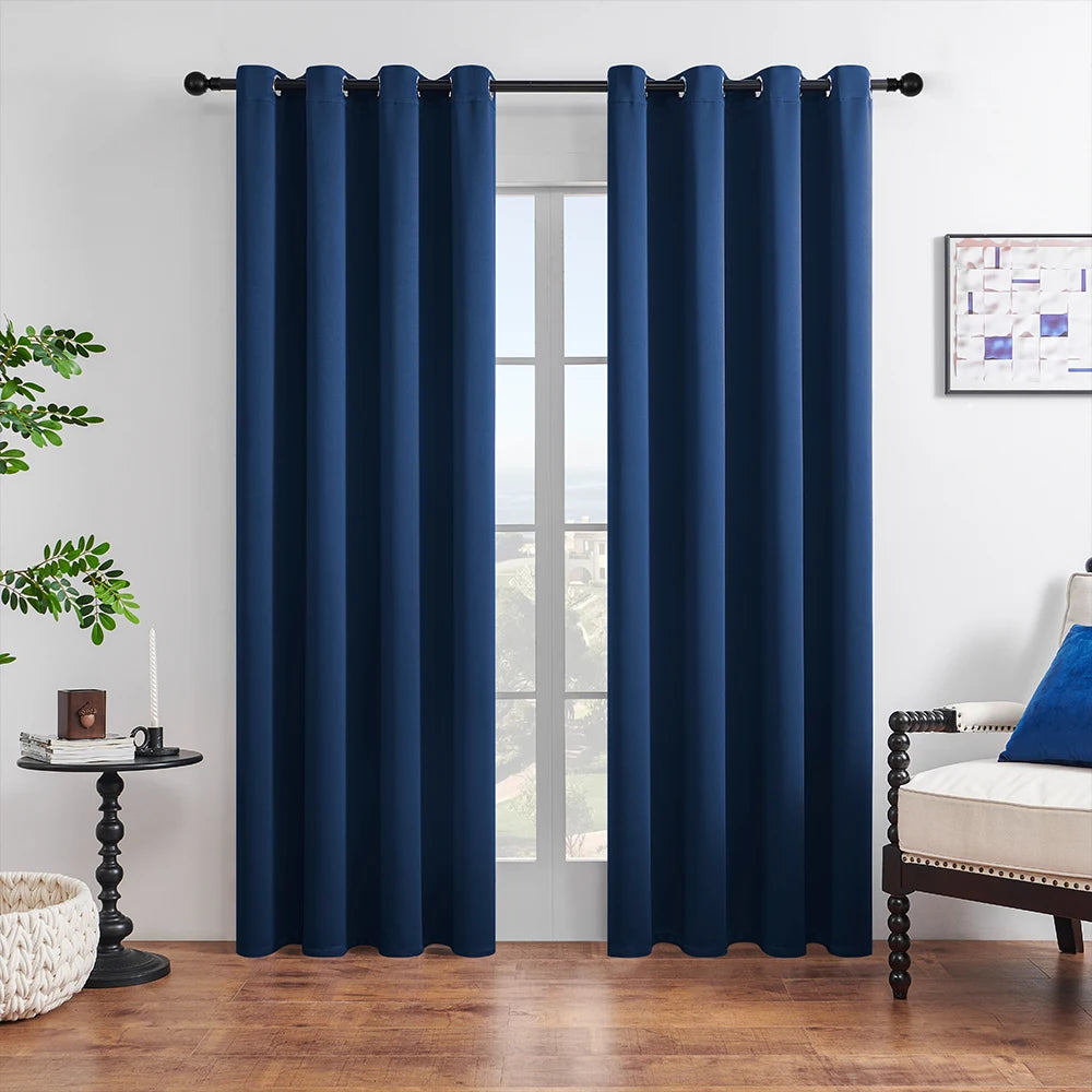 A set of dark blue blackout window curtains hanging on a black rod in a bright room.