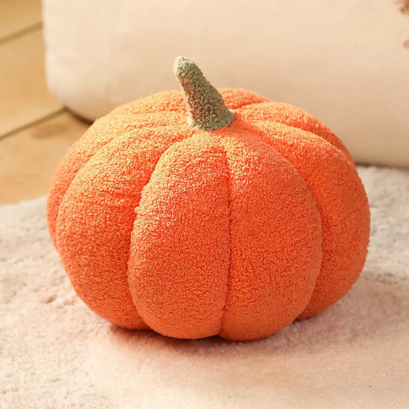 An orange plush pumpkin throw pillow with a green stem resting on a light surface.