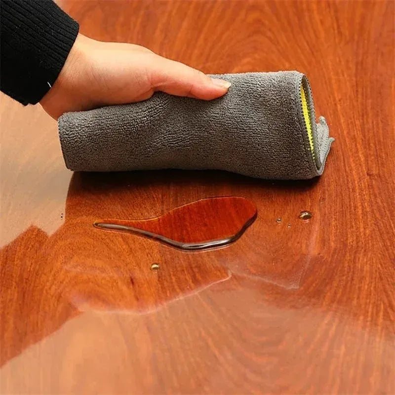 A hand is placing a gray, round waterproof PVC tablecloth onto a wooden table surface.