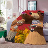 A fleece blanket featuring characters from the Masha cartoon, including a bear and a child, displayed on a sofa.