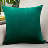 A deep emerald green velvet cushion cover resting on a light-colored sofa.