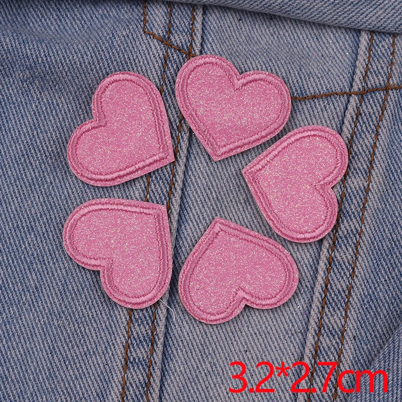 Five pink glitter heart star iron-on patches are laid out on a denim fabric.