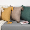 A collection of boho cotton linen throw pillow covers in mustard yellow, beige, and deep green resting on a gray fabric.