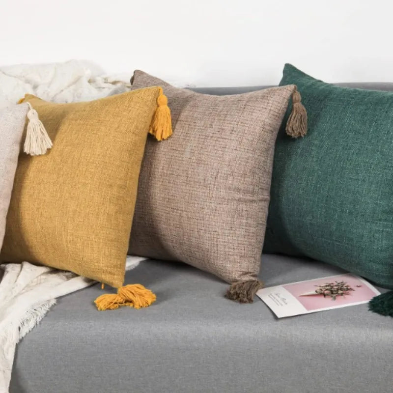 A collection of boho cotton linen throw pillow covers in mustard yellow, beige, and deep green resting on a gray fabric.
