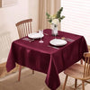 A deep burgundy satin tablecloth is set for dining with white plates and silverware, decorated with a floral arrangement.