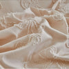 Close-up of a beige luxury quilt duvet set fabric featuring delicate lace trim and soft folds.