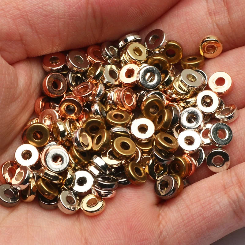 A handful of small, round acrylic flat spacer beads in various gold and silver tones held in a person's hand.