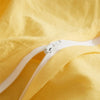 Close-up of a yellow duvet cover with a white zipper detail and pom-pom decoration.
