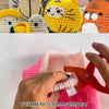 Hands are using orange crimping pliers to attach a safety eye to a pink crocheted item.