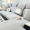 A light gray jacquard elastic sofa slipcover with decorative pillows and a patterned throw on a modern couch.