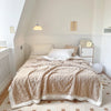 A beige thick fleece blanket is spread across a bed in a bright room.