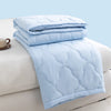 Light blue quilted duvet folded on a white surface with a cup nearby.