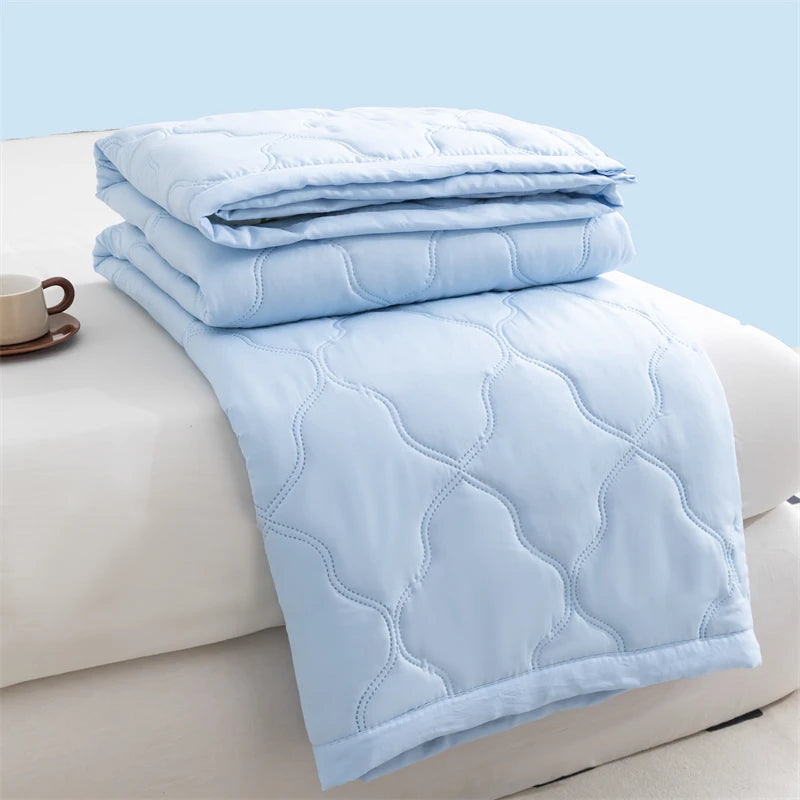 Light blue quilted duvet folded on a white surface with a cup nearby.
