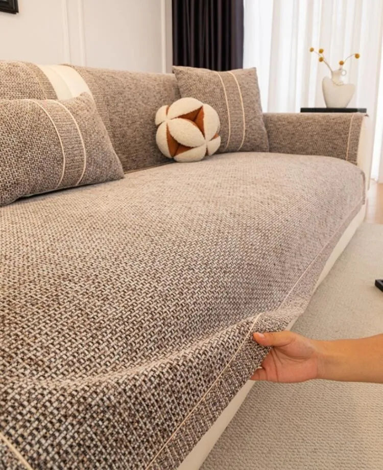 A close-up of a textured gray sofa cushion cover with decorative piping and a small cream-colored accent pillow.
