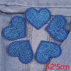 Five blue glitter heart shaped iron-on patches sewn onto denim fabric.