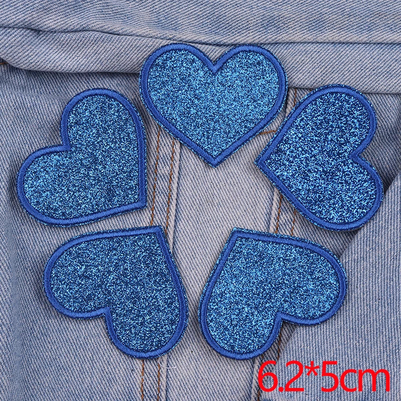 Five blue glitter heart shaped iron-on patches sewn onto denim fabric.