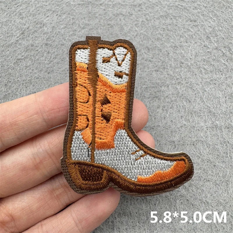 An embroidered iron-on patch shaped like a cowboy boot in brown and gray thread.