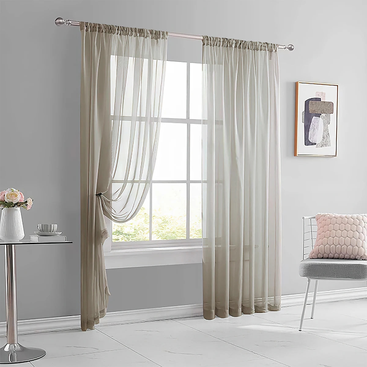 A pair of light beige sheer curtains hanging in a window frame in a modern living room setting.