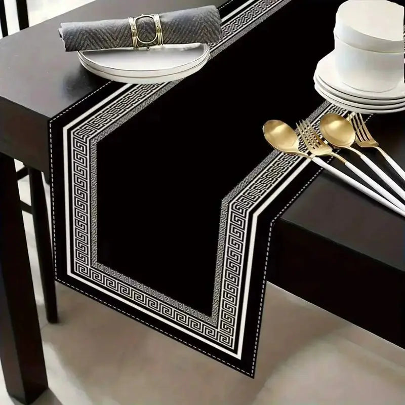 Black table setting featuring a geometric patterned placemat, a gray napkin, and gold silverware.
