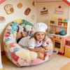 A young girl sits in a large colorful inflatable storage bag surrounded by kitchen play items and plush toys.